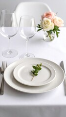 Elegant, minimalist table setting with white china, glassware, and a small sprig of greenery