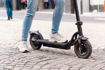 Person riding an electric scooter on a cobblestone street during the day in a bustling urban area...