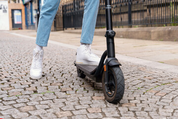 Person riding an electric scooter on a cobblestone street in a city during daytime with stylish...