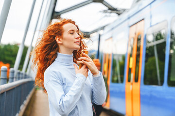 Red-haired woman enjoying the moment beside a bright blue train on a sunny day in an urban setting