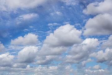 A bright sky filled with fluffy white cumulus clouds contrasting against a bright blue background