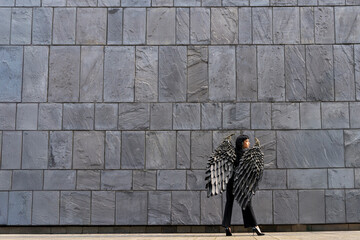 Fashion model posing with dramatic wings against a textured gray wall during a sunny afternoon in...