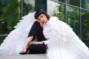 Model poses with large feathered wings in urban setting during daylight, showcasing fashion and...