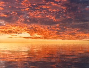 Dramatic and magnificent sunset seen above calm water and reflected in the ripples of the ocean surface