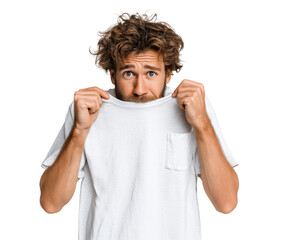A man with curly, dishevelled hair and a beard, looking surprised while pulling a white t-shirt up to his nose.