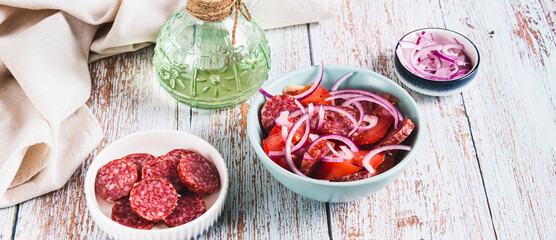 Delicious salad with chorizo, tomatoes and red onion in a bowl on the table web banner