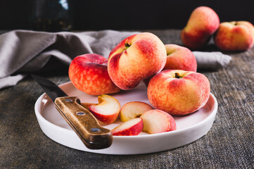 Whole and sliced peaches and a knife are placed on a plate on the table.
