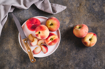 Whole and sliced peaches and a knife are placed on a plate on the table top view