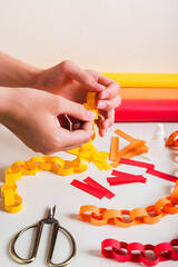 A girl's hands fold a strip of paper to make a paper chain vertical view