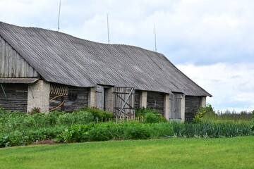 Old rustic wooden and brick barn with slanted roof, surrounded by lush green vegetable garden....