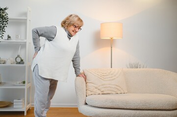Senior woman having backache and touching her back in living room at home