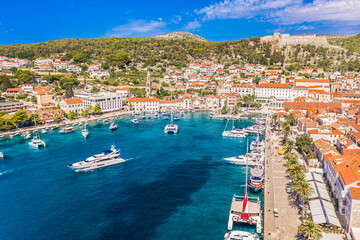Drone photo of Hvar town bathed in sunlight showing the full seafront, anchored boats, historic...