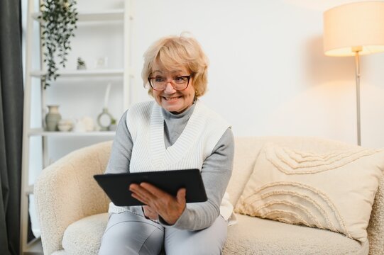 Head shot portrait close up happy mature woman using computer tablet, looking at camera, laughing at funny joke or video in social network