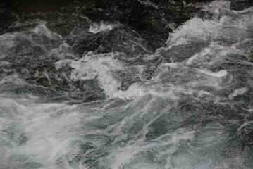 Dynamic close-up of fast-moving river water with swirling foam and ripples, capturing the raw energy and texture of natural fluid motion.