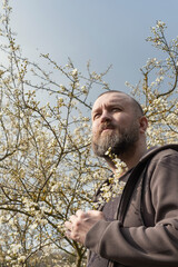 Man with beard stands thoughtfully among flowering trees