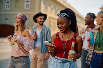 Happy black woman using cell phone while going to summer music festival with friends.