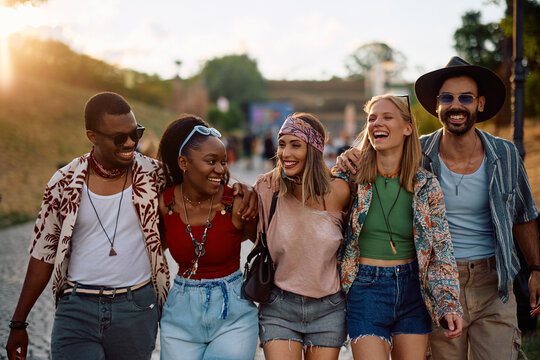 Group of carefree friends walking embraced while going to summer music festival.