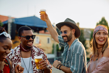 Happy festival goer and his friends drinking beer and dancing at sunset.