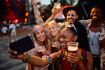 Happy black woman and her friends taking selfie while attending summer music festival in summer.