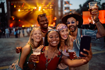 Happy black woman using cell phone while taking selfie with friends on open air music concert.