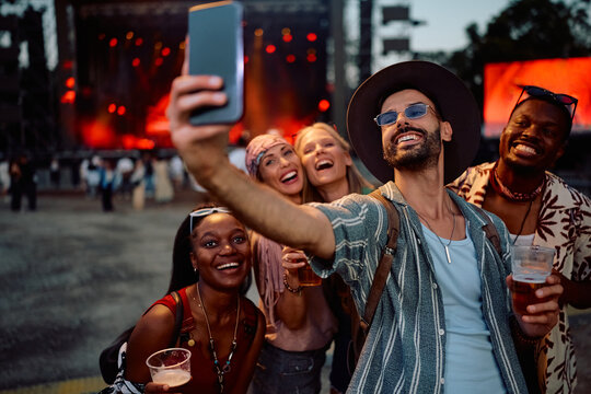 Happy festival goers talking selfie in front of music stage during summer festival.