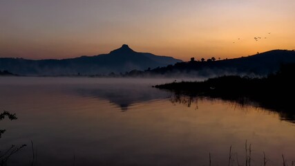 Navi Mumbai Golden hour landscape showing calm lake waters reflecting mountain silhouettes under a misty dawn sky in the Western Ghats, India. A tranquil, ideal for nature and travel themes. - Powered by Adobe