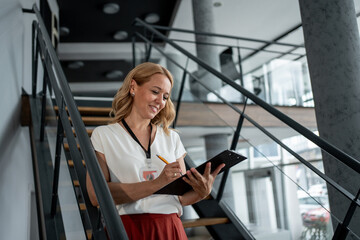 Businesswoman taking notes on clipboard while standing on stairs in office building