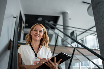 Smiling businesswoman walking upstairs holding clipboard and pen