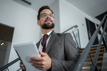 Businessman walking up stairs holding digital tablet and looking upwards