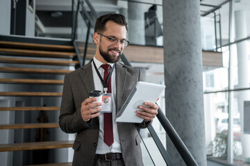 Smiling businessman using digital tablet and holding coffee in office building