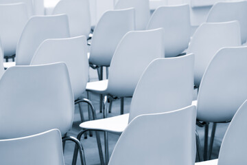 Row of white chairs are empty. There are at least 15 chairs in the row. The chairs are all facing...