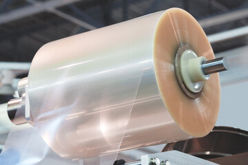 A machine with a roll of polyethylene plastic wrapping film on it. The machine is in a factory....