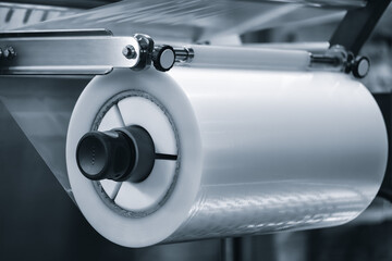 A machine with a roll of polyethylene plastic wrapping film on it. The machine is in a factory....