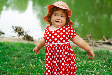 Little Girl in a Polka Dot Dress Enjoys Nature by the Water During a Sunny Day