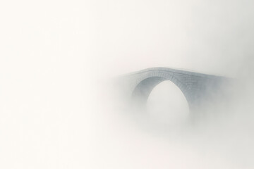 A stone bridge disappearing in a thick fog against a light background. Space for text.