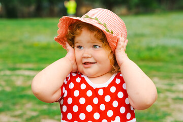 Smiling Child in Red Polka Dot Dress and Pink Hat Enjoys Sunny Day Outdoors in Green Park Setting
