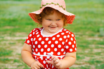 Smiling Child in Red Polka Dot Dress and Pink Hat Enjoys Sunny Day Outdoors in Green Park Setting