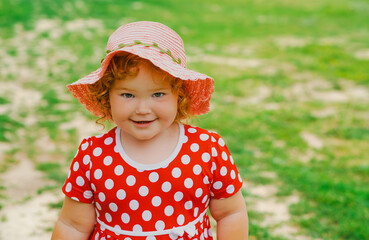 Smiling Child in Red Polka Dot Dress and Pink Hat Enjoys Sunny Day Outdoors in Green Park Setting