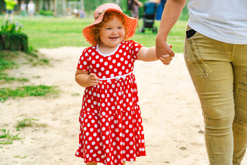 Little Girl in a Red Polka Dot Dress Enjoys a Sunny Day at the Park While Holding Hands With an Adult