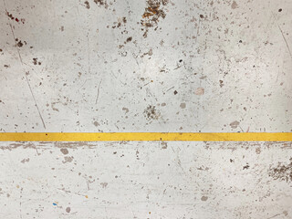 Floor of an an arts studio covered in various drops and splashes of paint marks and a yellow stripe