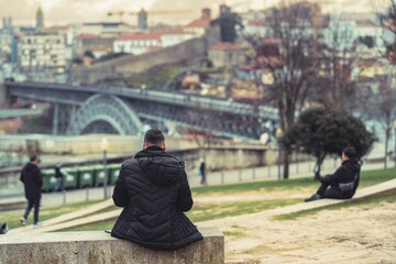A person sits on a ledge, contemplating the cityscape of Porto and the iconic Ponte Luis I bridge....