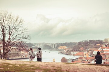 Two travelers admire the Douro River and city skyline. A lone figure sits nearby, absorbed in the...