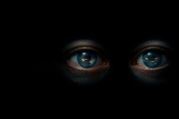 Blue eyes on a black background with the reflection of light. Space for text.