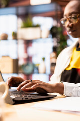Freelancer inputting data on laptop, completing spreadsheets in apartment workspace. African...