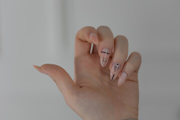 Elegant almond nails with beige gel polish, close-up of glamorous feminine hands in soft light.