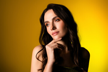 Stunning young woman with long brunette hair posing on a vibrant yellow background in a stylish...