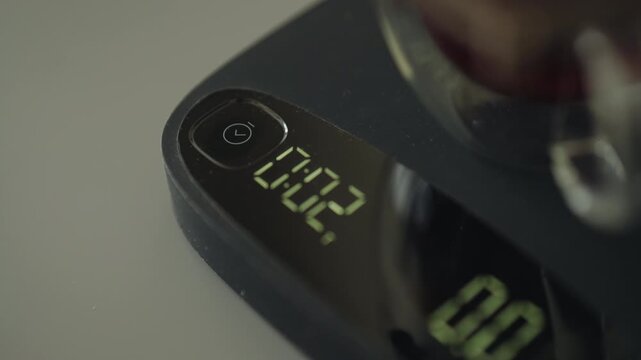 Man using kitchen scale to accurately measure coffee, pushing tare button to zero scale, ensuring precise coffee brewing, close-up. Process of making freshly brewed coffee at home, slow motion.
