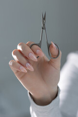 Close-up of manicure scissors in hand with elegant beige manicure, professional salon work