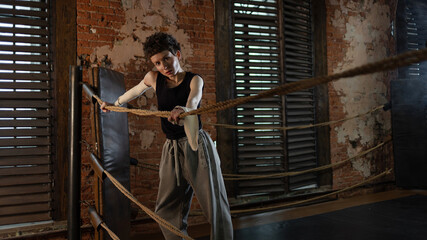Short-haired boxer pausing workout, leaning on ring ropes with cinematic intensity
