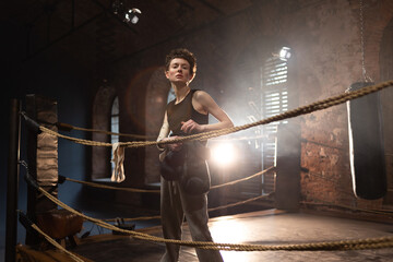 Boxer woman with short hair pausing on ropes, cinematic gym training atmosphere